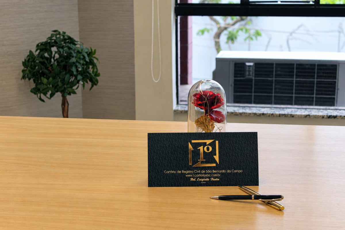 Mesa com identificação do cartório, canetas e rosa sob uma cúpula de vidro